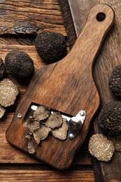 Shaver with whole and sliced black truffles on wooden table, flat lay