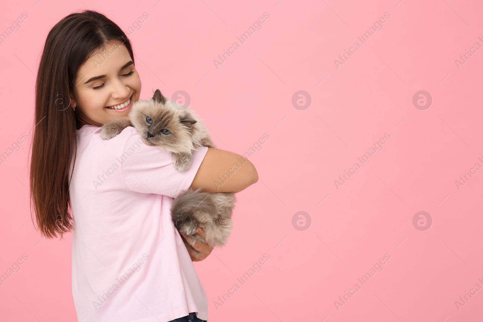 Photo of Happy woman hugging her cute cat on pink background, space for text