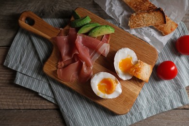 Delicious breakfast with soft boiled egg and tasty prosciutto served on wooden table, flat lay