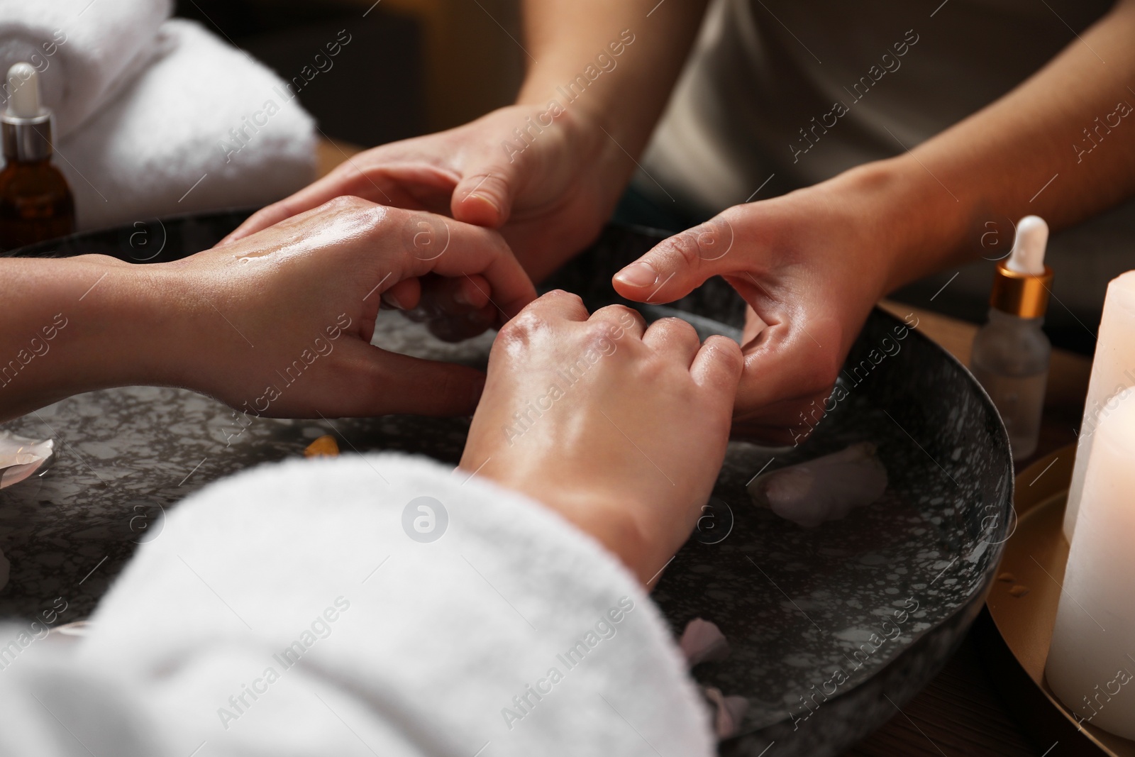 Photo of Woman receiving hand massage in spa salon, closeup. Bowl of water and flower petals on table