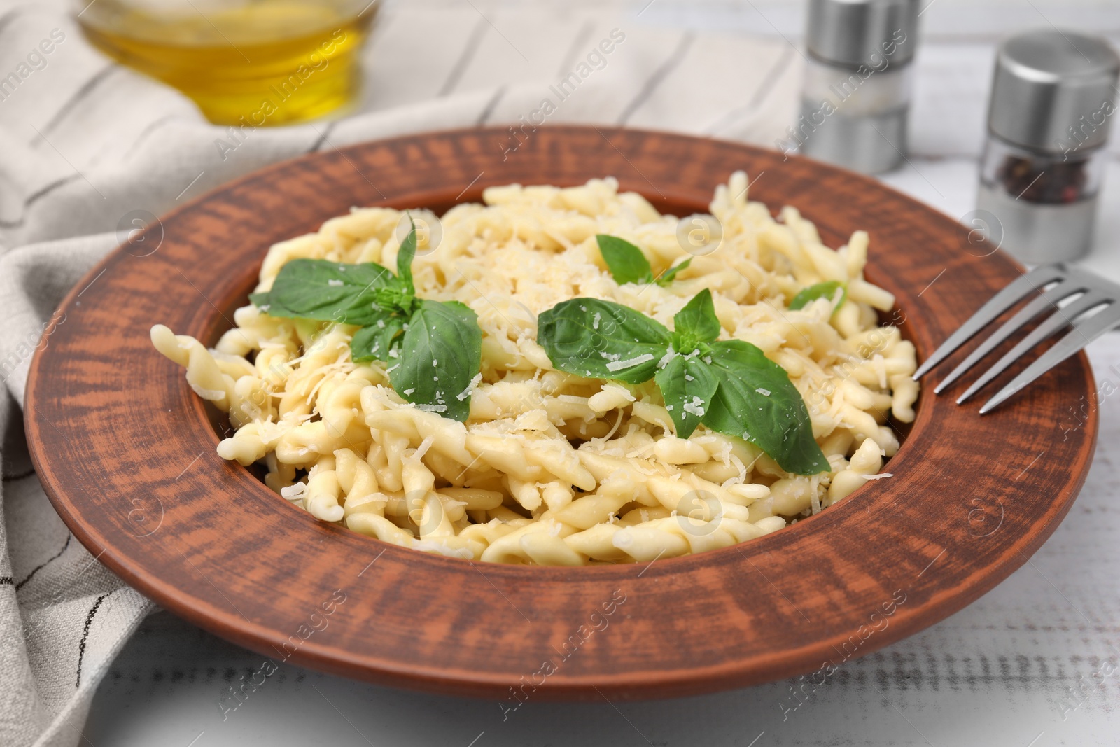 Photo of Plate of delicious trofie pasta with cheese and basil leaves on white wooden table