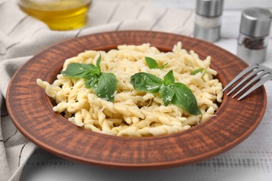 Photo of Plate of delicious trofie pasta with cheese and basil leaves on white wooden table