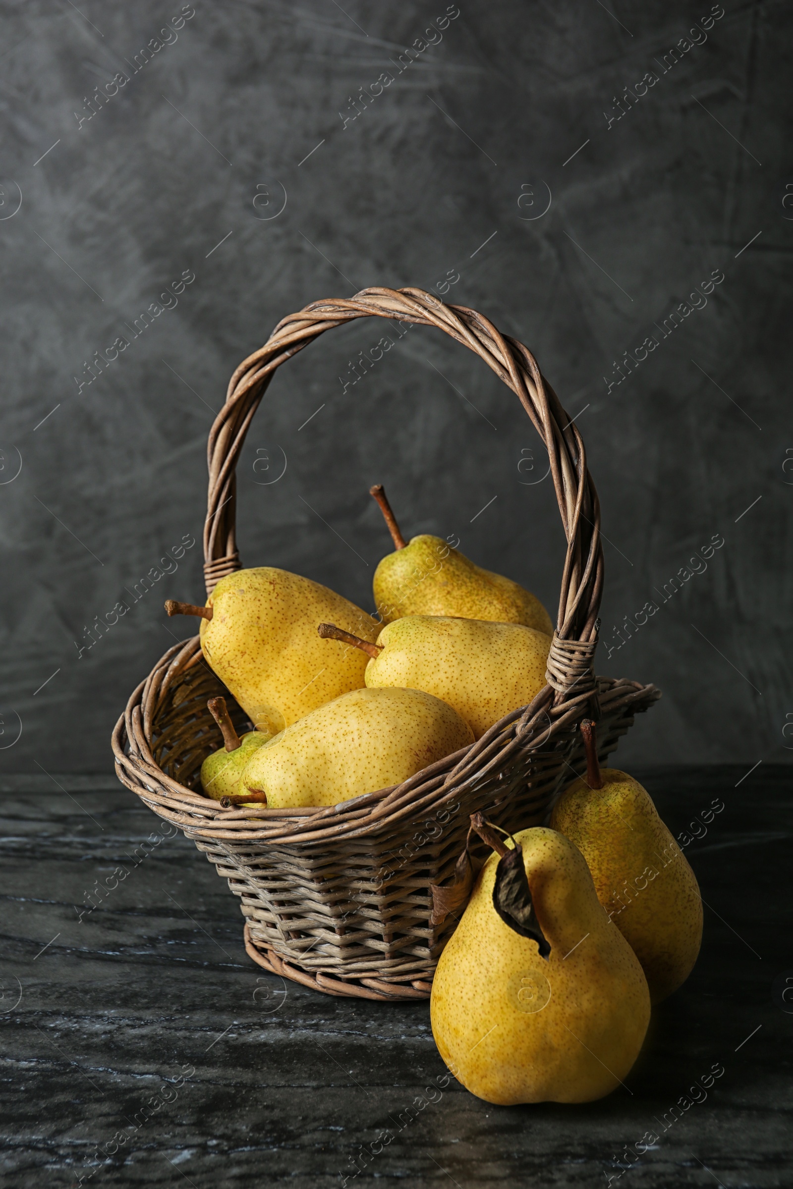 Photo of Basket with fresh ripe pears on table against gray background