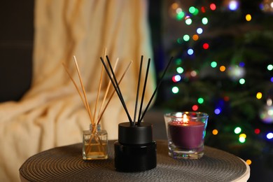 Aromatic reed air fresheners and candle on side table in cozy room