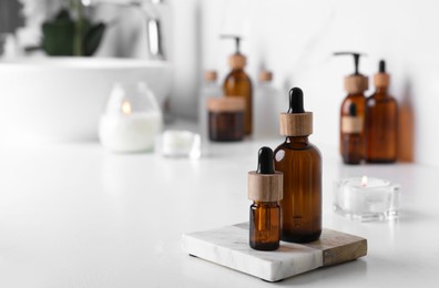 Photo of Bottles of essential oil on white countertop in bathroom. Space for text