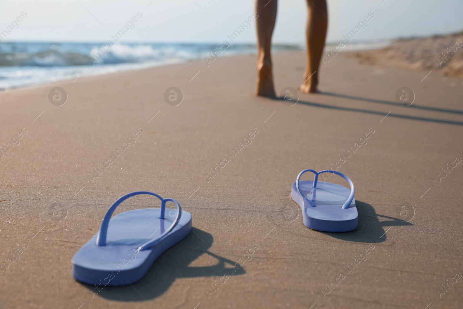 Photo of Woman left her beach slippers and walking barefoot on sandy seashore, closeup