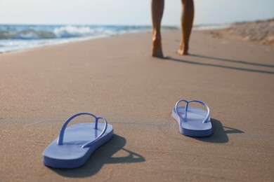 Photo of Woman left her beach slippers and walking barefoot on sandy seashore, closeup