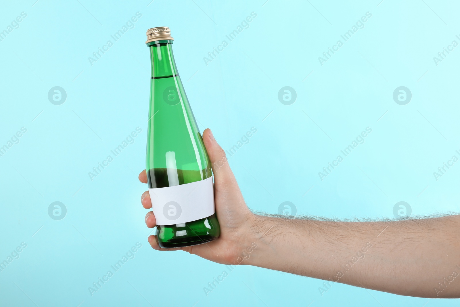 Photo of Man holding glass bottle of pure water with blank tag on color background