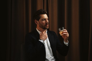 Photo of Man in suit holding glass of whiskey with ice cubes on brown background