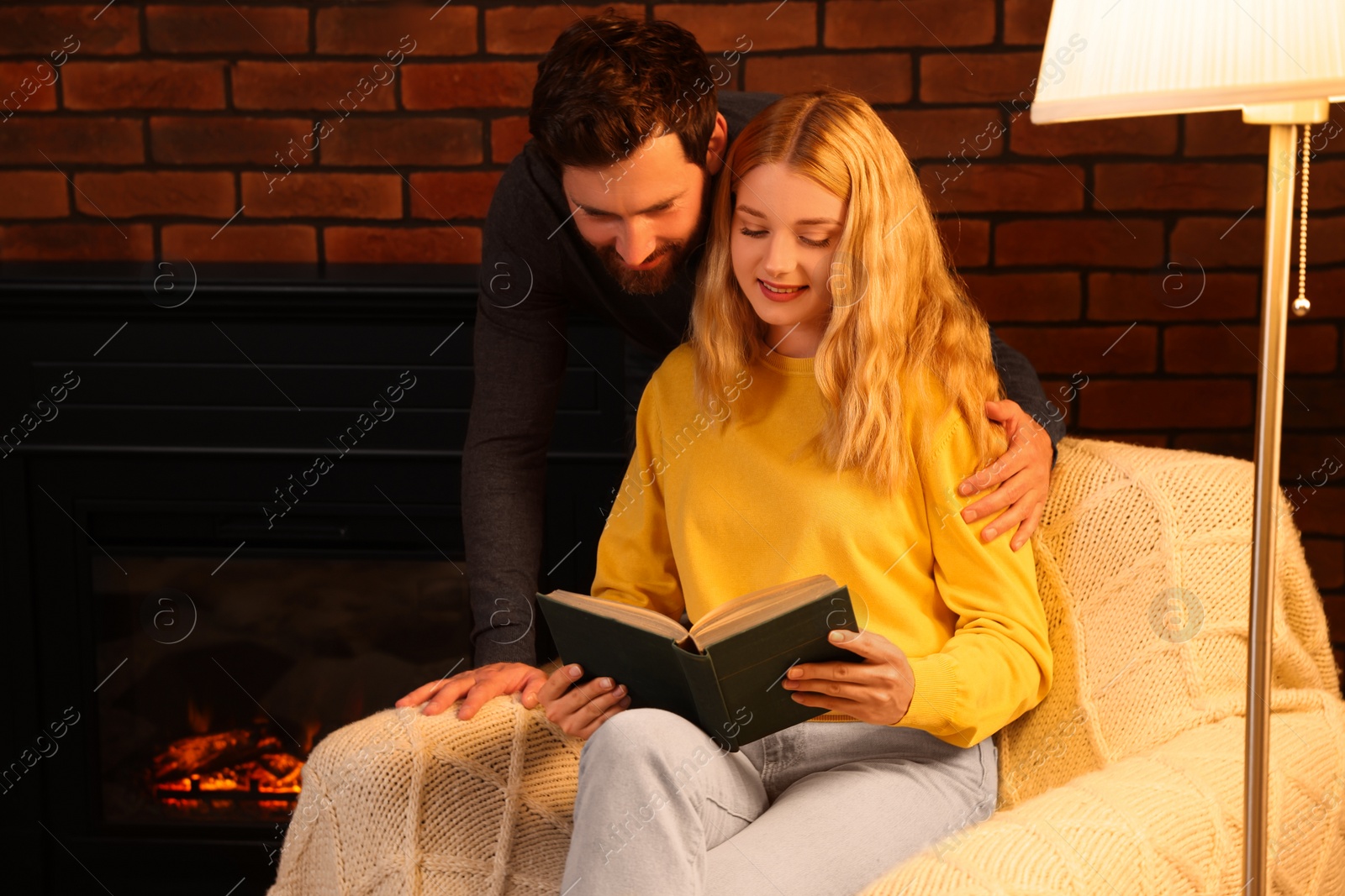 Photo of Lovely couple reading book near fireplace at home