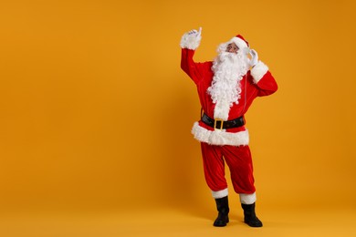 Photo of Merry Christmas. Santa Claus in headphones listening to music on orange background, space for text