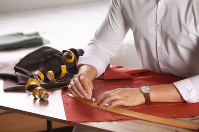 Photo of Tailor working with cloth at table in atelier