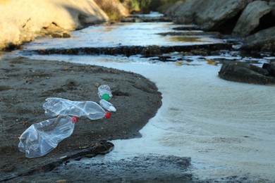 Photo of Used plastic bottles near water at beach, space for text. Environment pollution