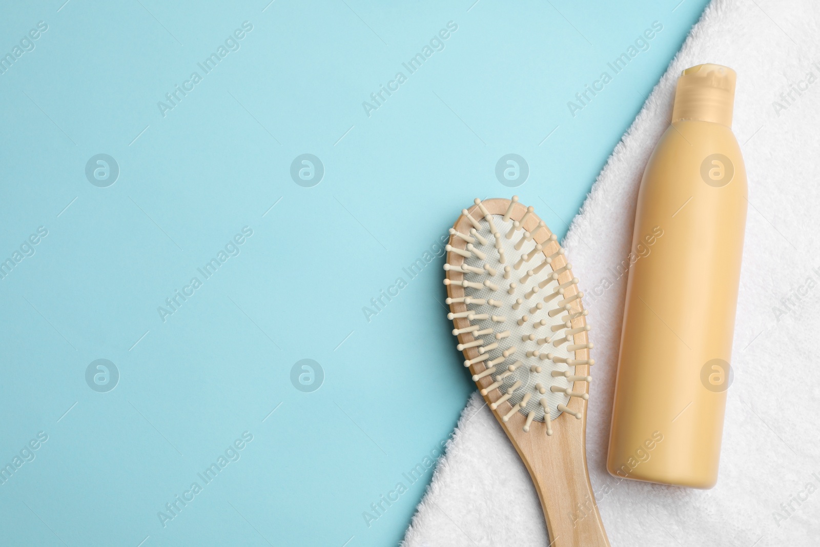Photo of Flat lay composition with brush and shampoo bottle on light blue background, space for text. Hair care cosmetics