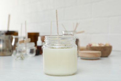 Photo of Glass jar with wax and wick on white table. Making homemade candle