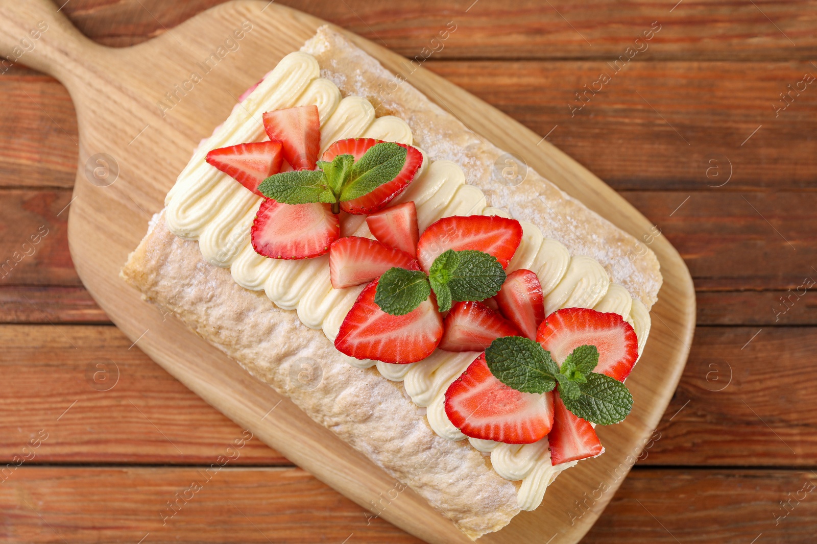 Photo of Delicious cake roll with strawberries and cream on wooden table, top view