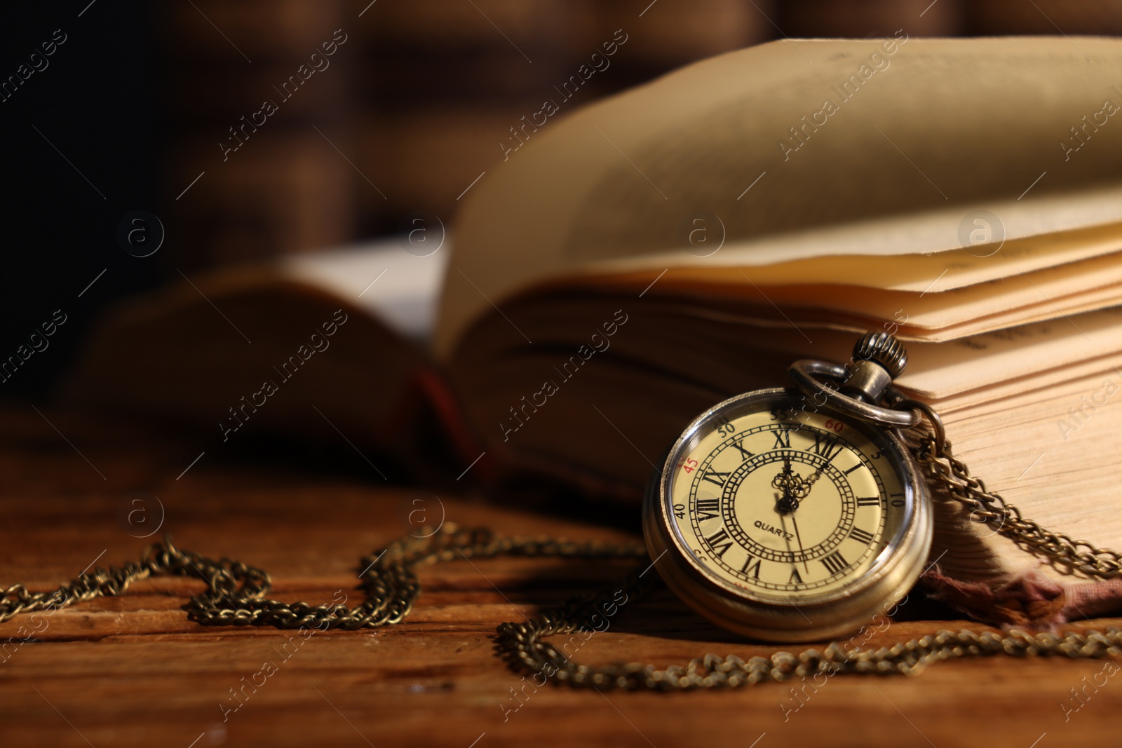 Photo of Pocket clock with chain and book on wooden table, closeup. Space for text