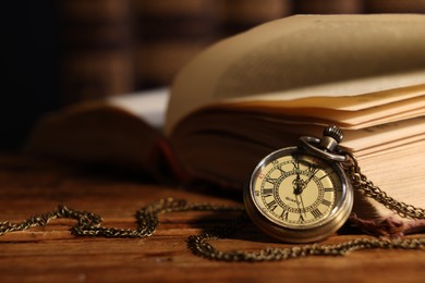 Pocket clock with chain and book on wooden table, closeup. Space for text