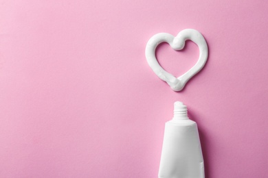 Photo of Heart shape made of toothpaste near tube and space for text on color background, top view