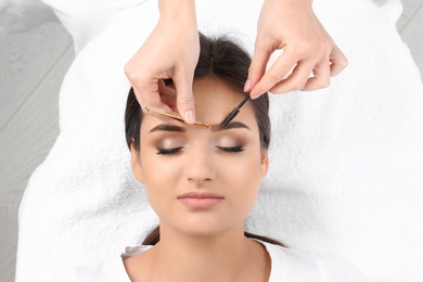 Photo of Young woman having professional eyebrow correction procedure in beauty salon