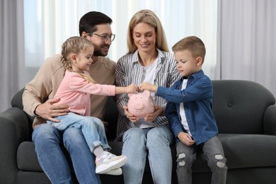 Family budget. Children putting coins into piggy bank while their parents watching at them indoors