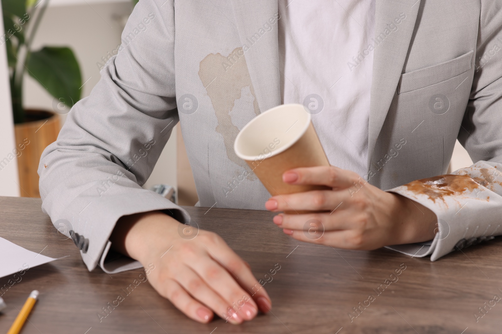 Photo of Woman showing stain from coffee on her jacket at wooden table indoors, closeup