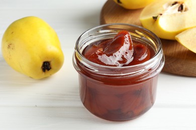 Tasty homemade quince jam in jar and fruits on white wooden table, closeup
