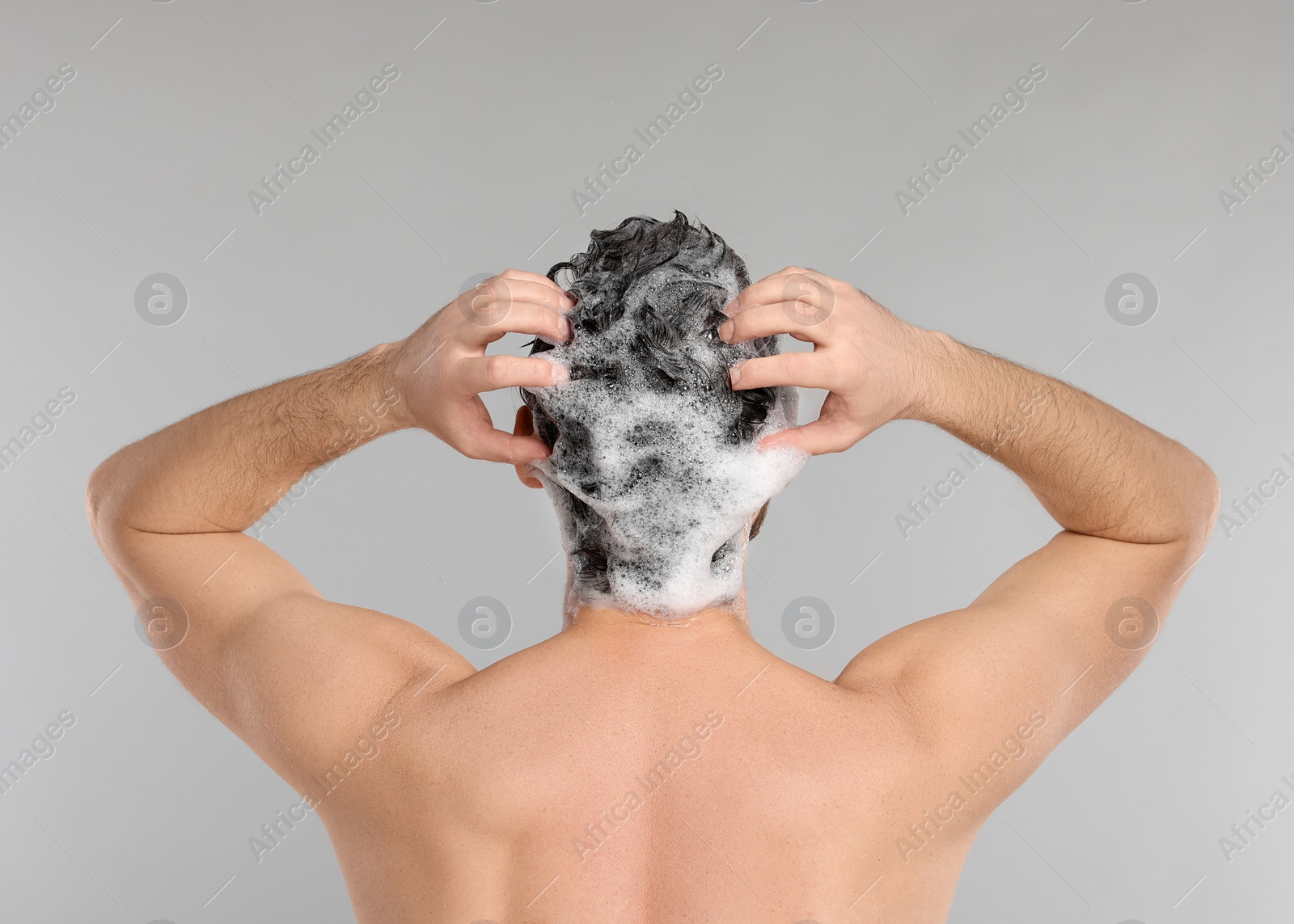 Photo of Man washing his hair with shampoo on grey background, back view