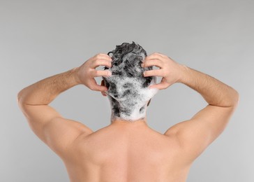 Photo of Man washing his hair with shampoo on grey background, back view