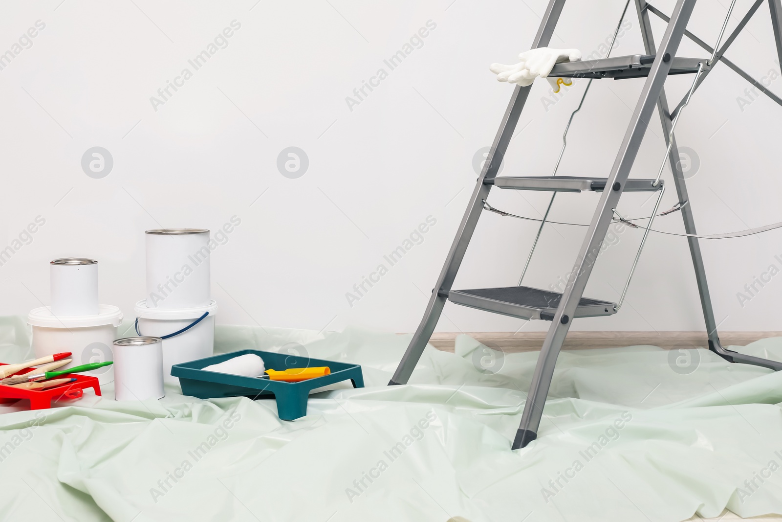 Photo of Metallic folding ladder and painting tools indoors, space for text