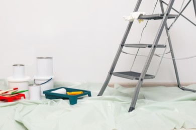 Photo of Metallic folding ladder and painting tools indoors, space for text