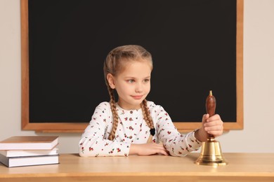 Photo of Pupil with school bell sitting at desk near chalkboard in classroom