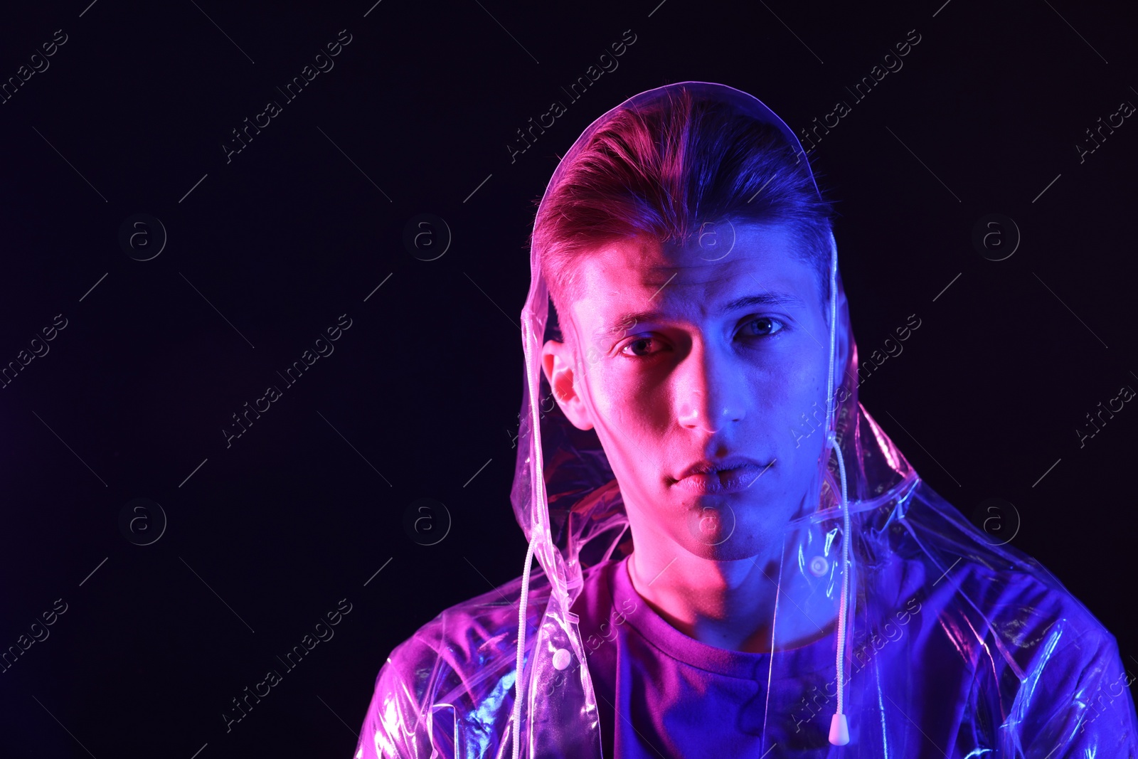 Photo of Young man wearing clear coat on dark background in neon lights. Space for text