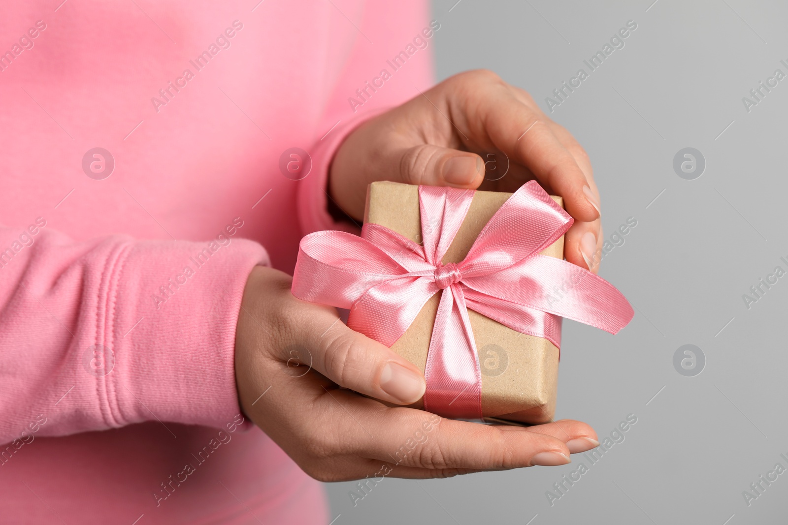 Photo of Woman holding gift box with pink bow on light grey background, closeup