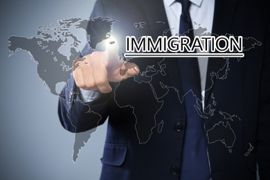 Image of Businessman touching word IMMIGRATION on virtual screen against grey background, closeup