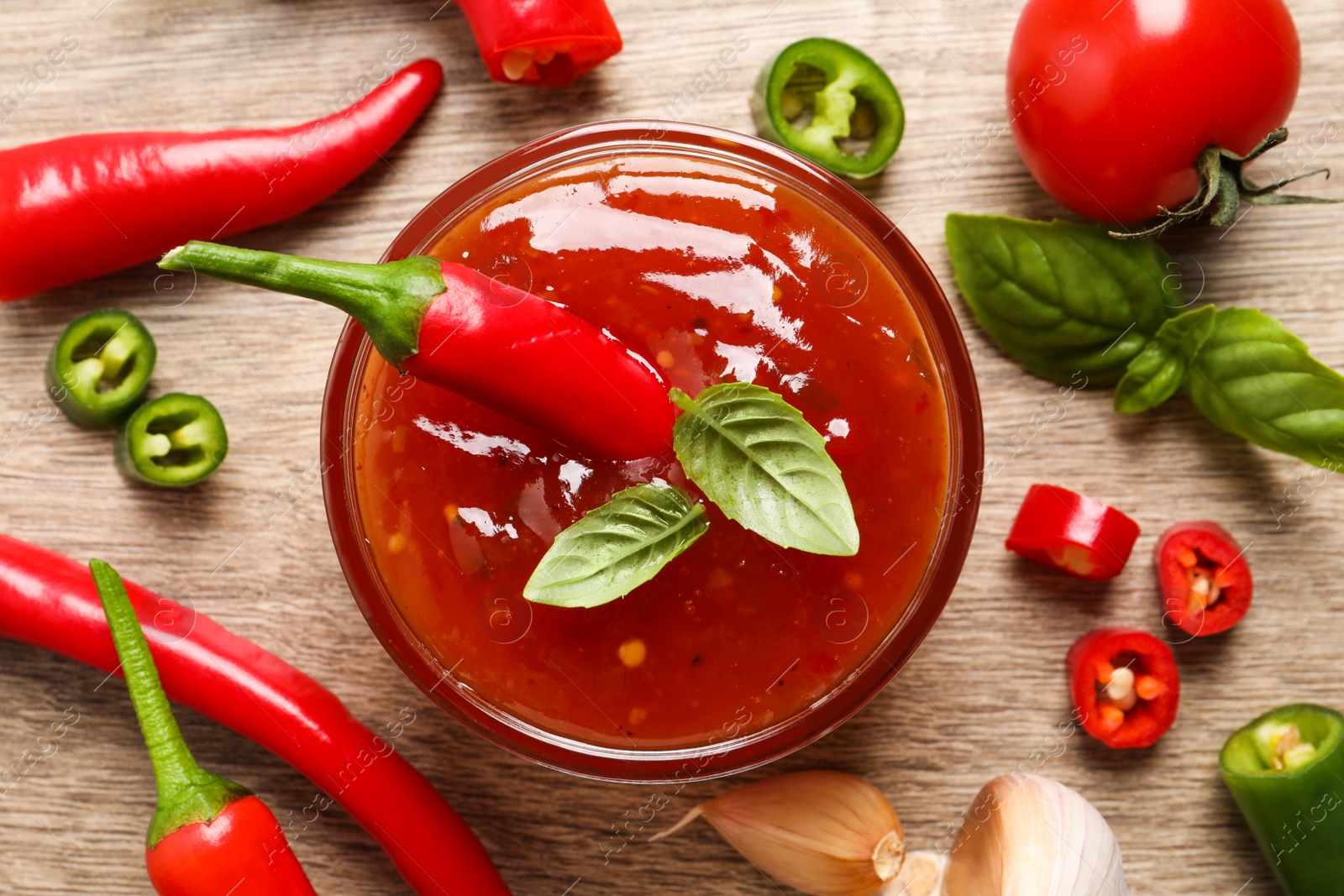 Photo of Spicy chili sauce and ingredients on wooden table, flat lay