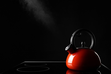 Modern kettle with whistle on stove against black background, space for text