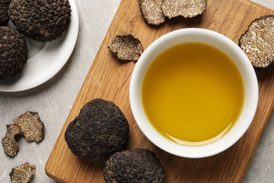 Photo of Fresh truffles and oil in bowl on light grey table, flat lay