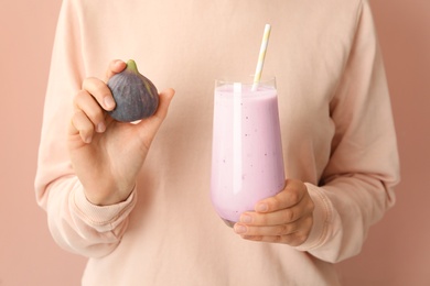 Woman holding smoothie and fresh fig on pink background, closeup