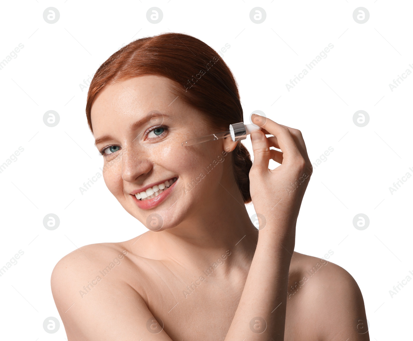 Photo of Smiling woman with freckles applying cosmetic serum onto her face on white background