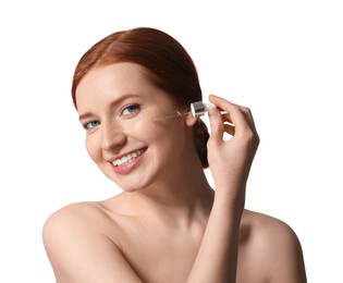 Smiling woman with freckles applying cosmetic serum onto her face on white background