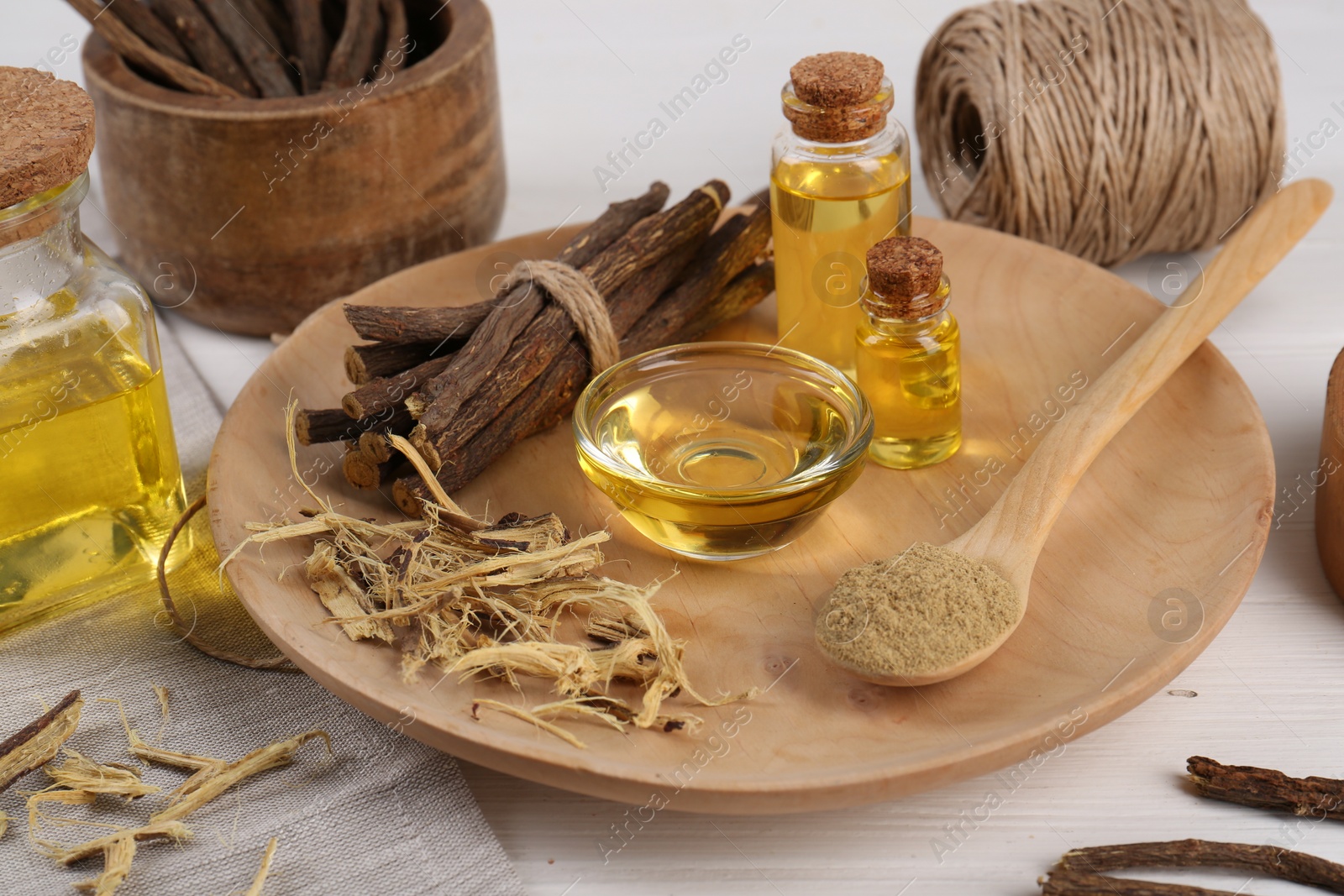 Photo of Dried sticks of licorice roots, powder and essential oil on white wooden table