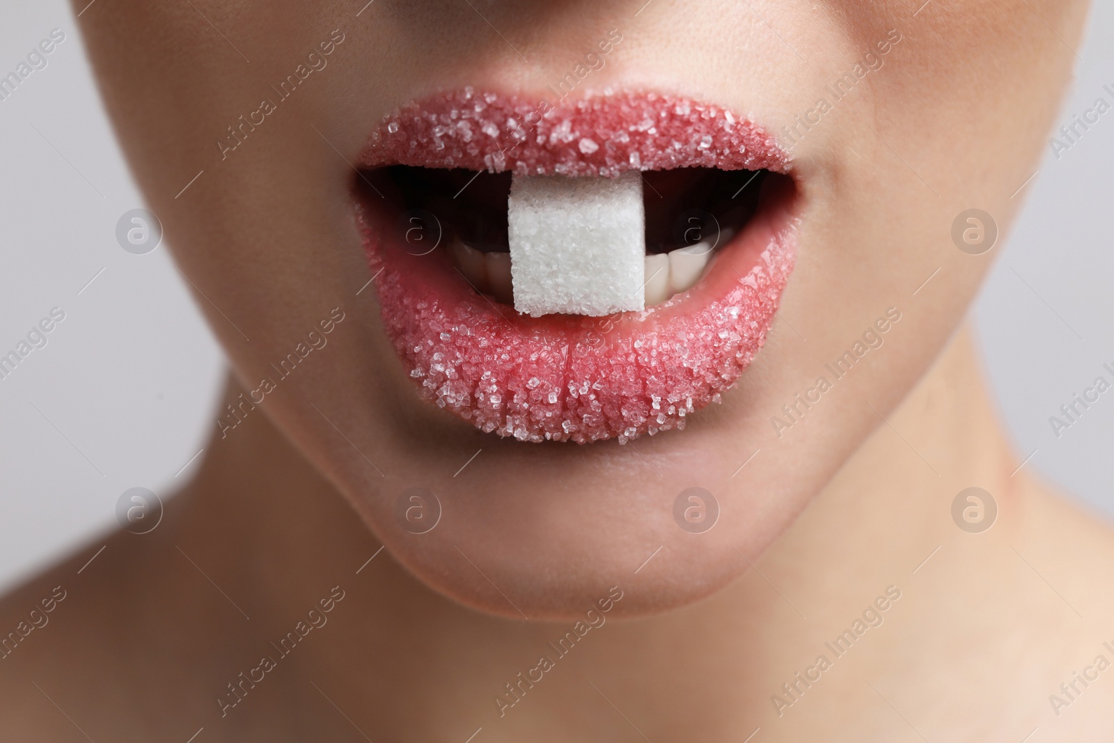 Photo of Closeup view of young woman with beautiful lips eating sugar cube on light grey background