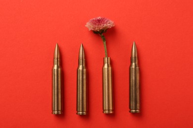 Photo of Bullets and cartridge case with beautiful flower on red background, flat lay