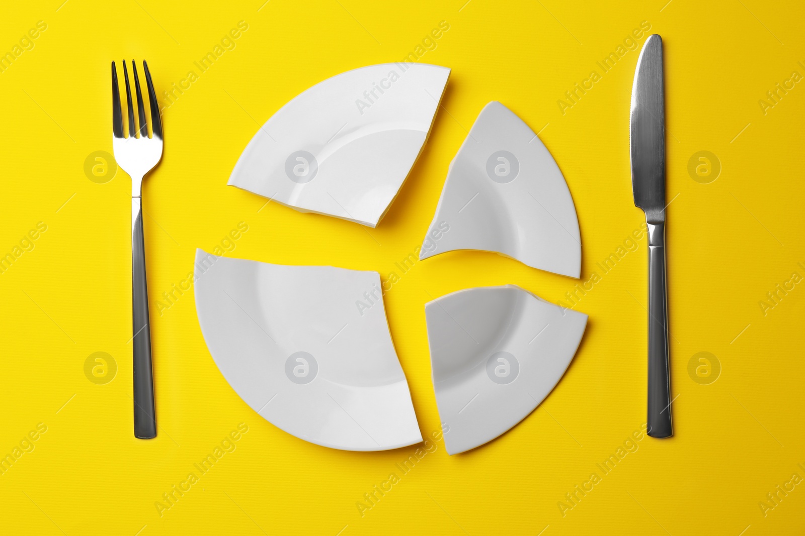 Photo of Pieces of broken white ceramic plate and cutlery on yellow background, flat lay