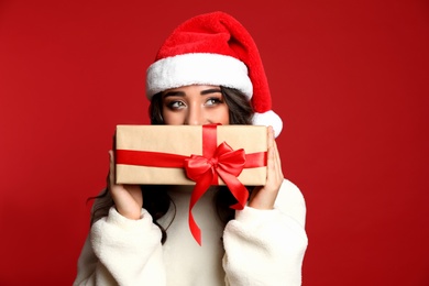 Photo of Beautiful woman in Santa hat with Christmas gift on red background