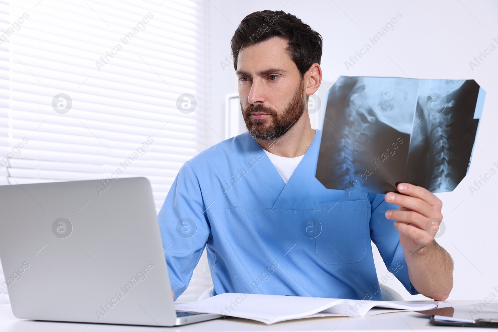 Photo of Doctor holding neck MRI scan and working on laptop in hospital