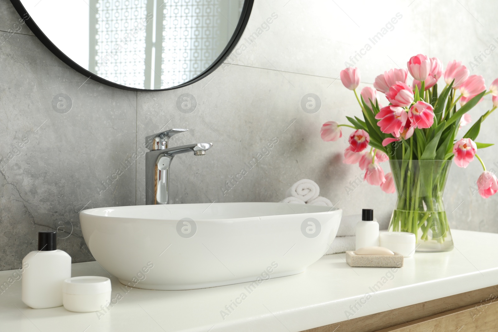 Photo of Vase with beautiful pink tulips and toiletries near sink in bathroom