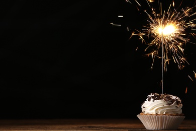 Photo of Delicious dessert with burning sparkler on wooden table against dark background, space for text