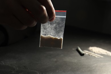 Photo of Drug addiction. Man with plastic bag of cocaine at grey table, closeup